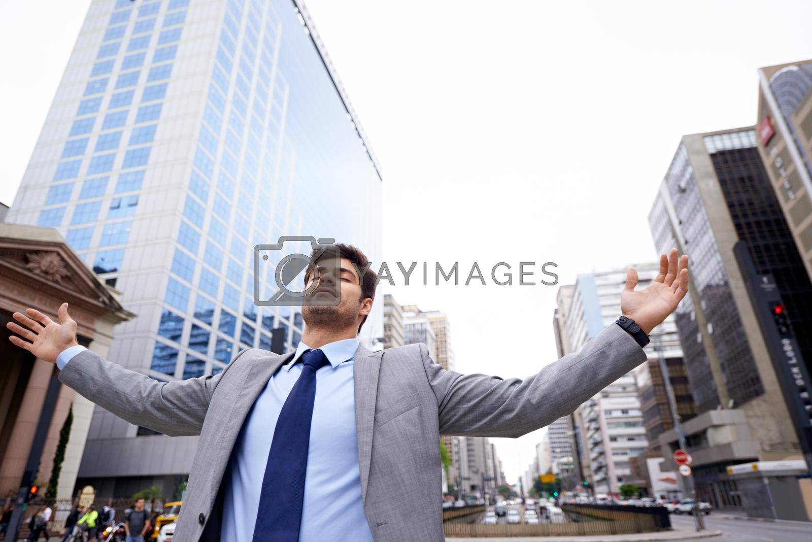 Royalty free image of Theres no place like the city. A contented young businessman standing in the city with his eyes closed and his arms raised. by YuriArcurs