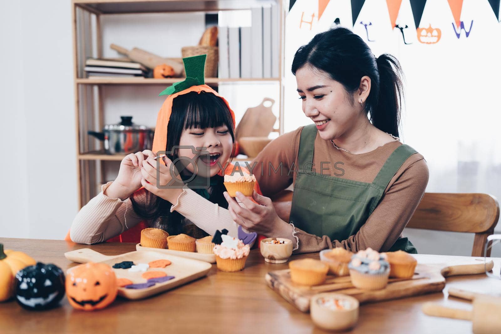Royalty free image of Young girl and mother at Halloween making treats and cupcake on table. Happy Halloween day by itchaznong