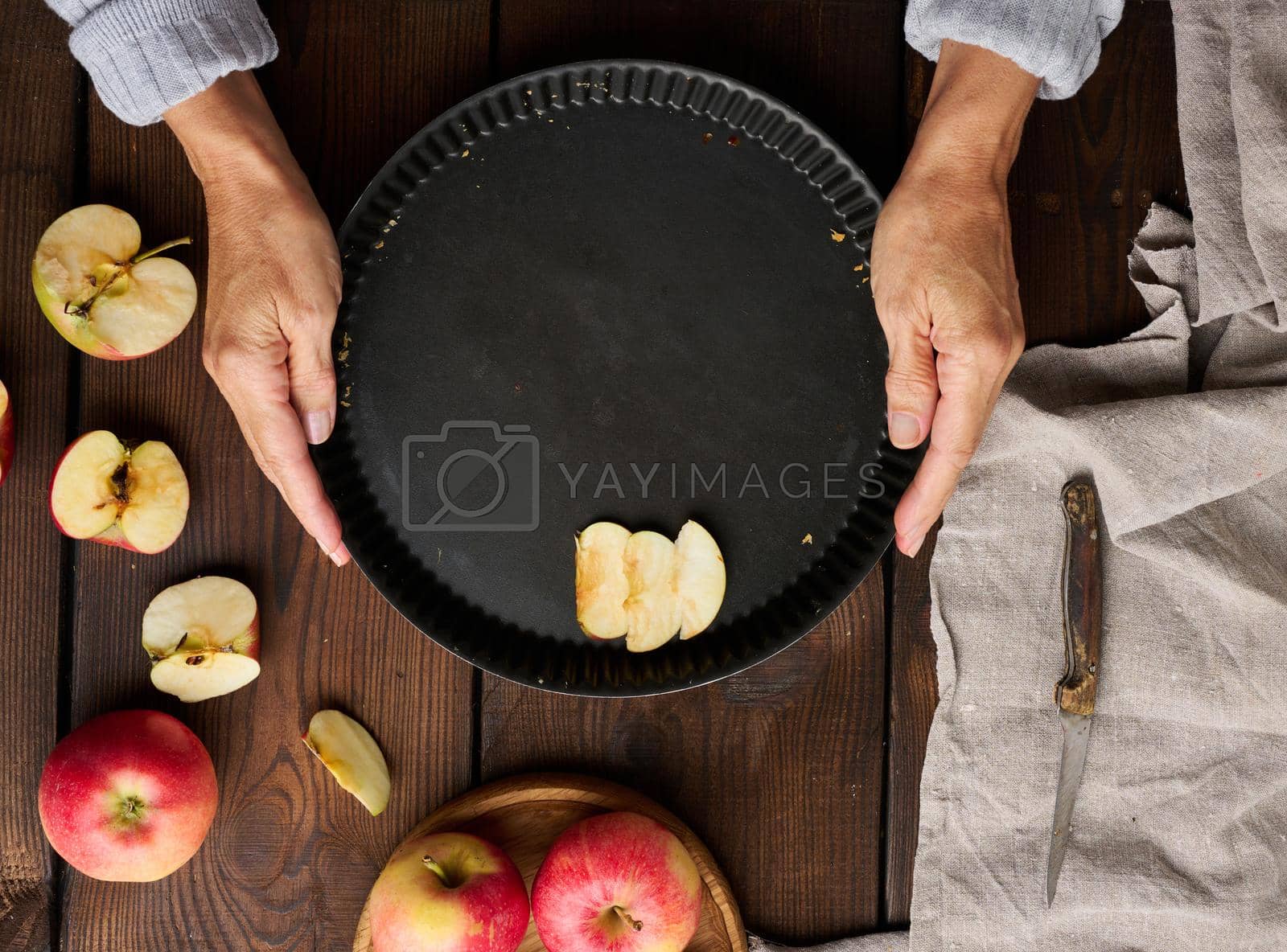 Royalty free image of A woman puts apple slices in a round baking sheet on the table, next to the ingredients. View from above by ndanko