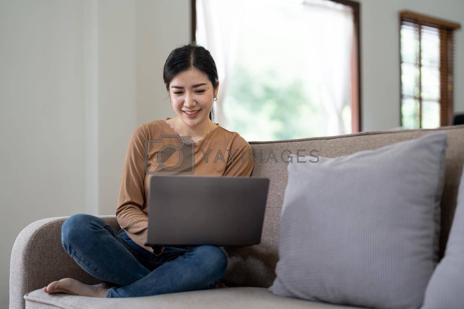 Royalty free image of Happy asian woman using laptop in the sofa with a happy face standing and smiling with a confident smile showing teeth by nateemee