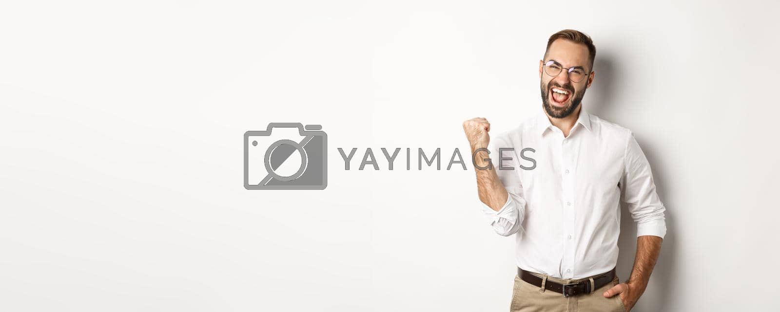 Royalty free image of Successful businessman rejoicing, making fist pump and saying yes, achieve goal, standing over white background by Benzoix