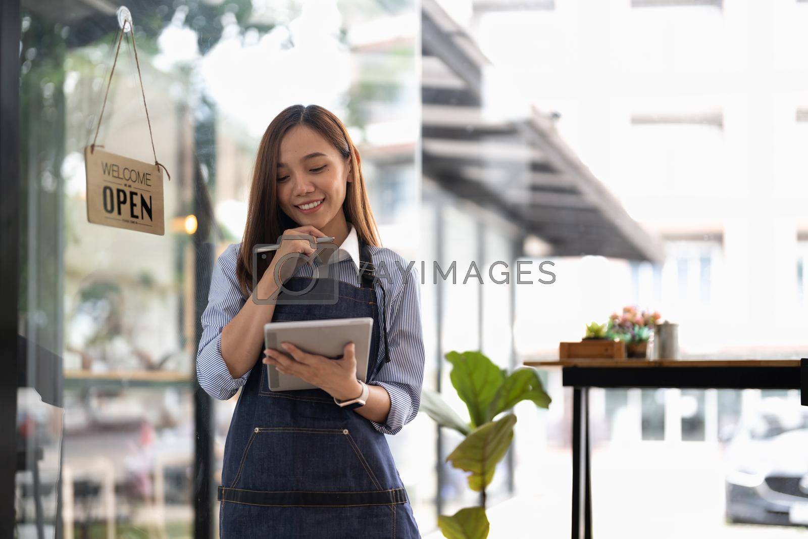 Royalty free image of Young asian woman coffee shop owner wearing apron holding digital tablet ready to receive orders. by nateemee