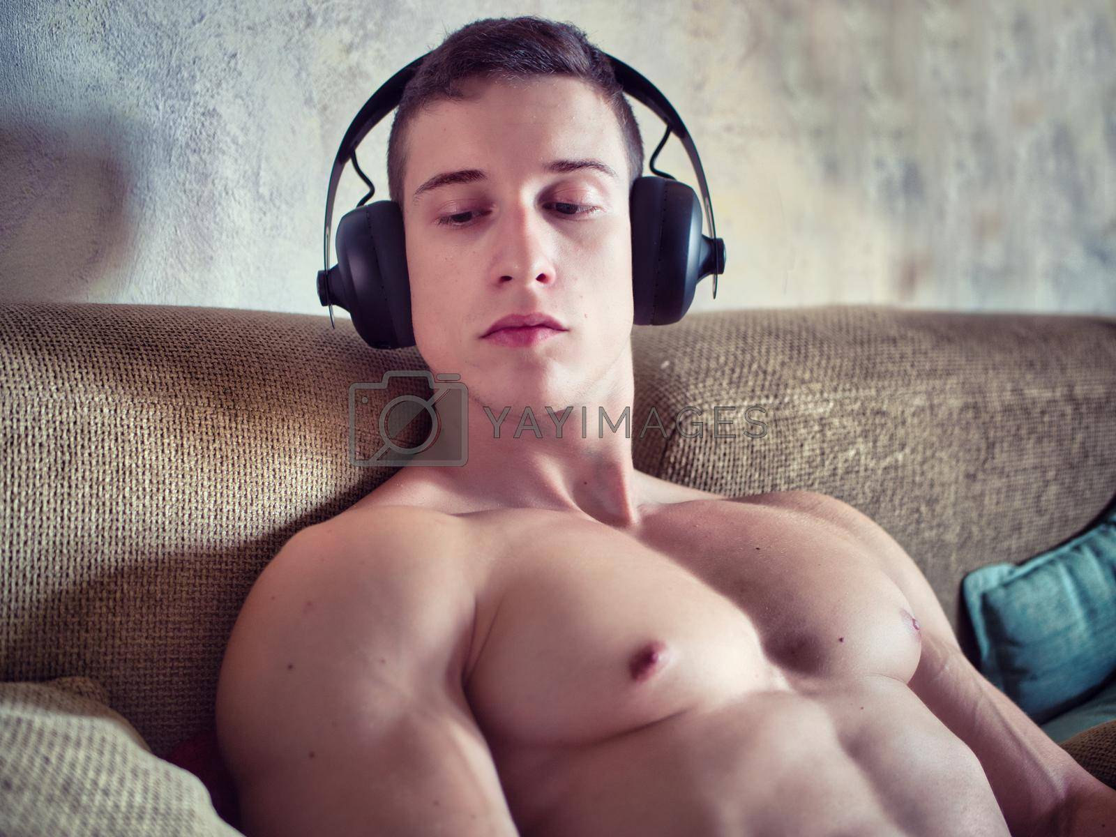 Royalty free image of Male bodybuilder listening to music on sofa by artofphoto