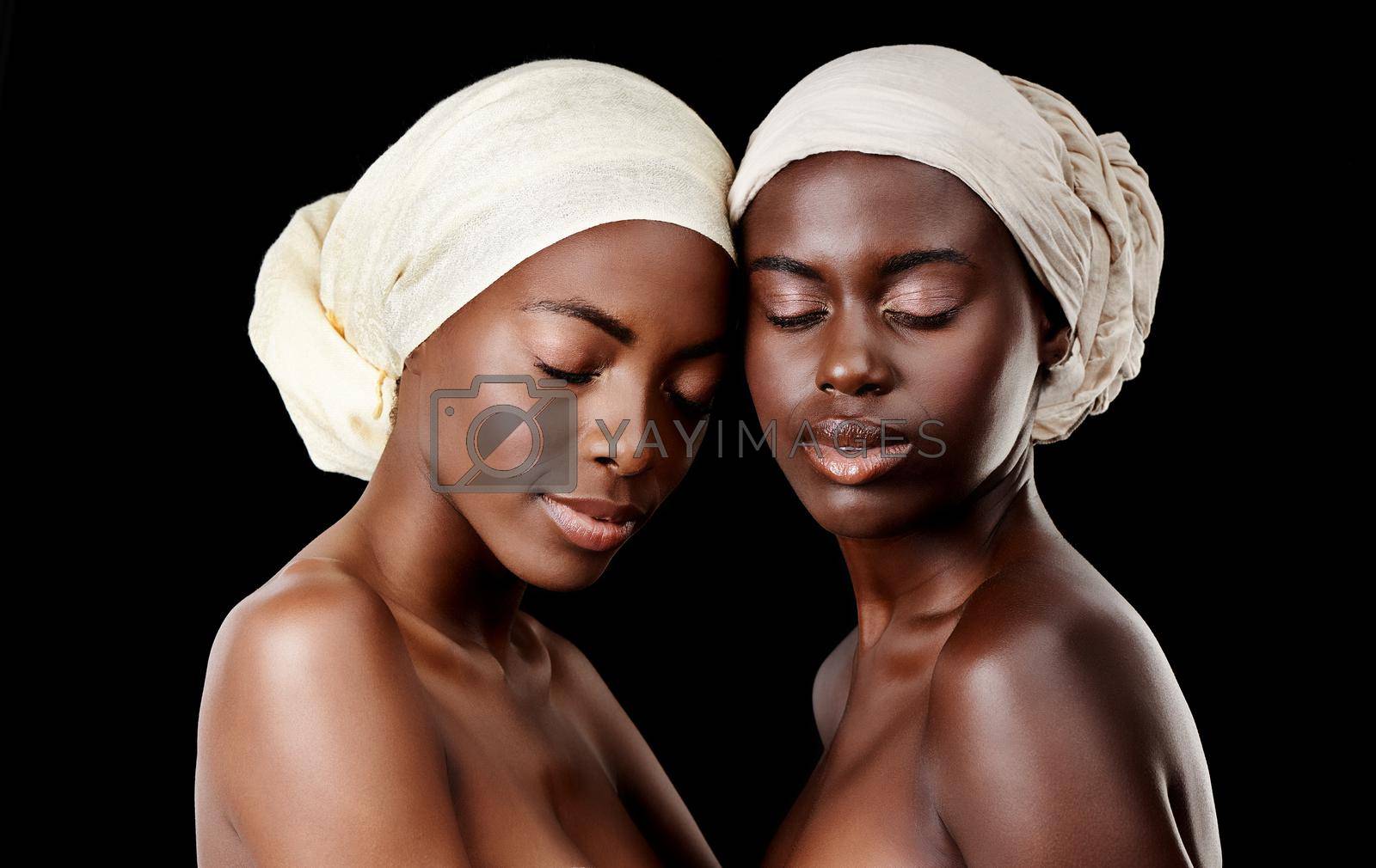 Royalty free image of Two peas in a pod. Studio shot of two beautiful women wearing headscarves against a black background. by YuriArcurs