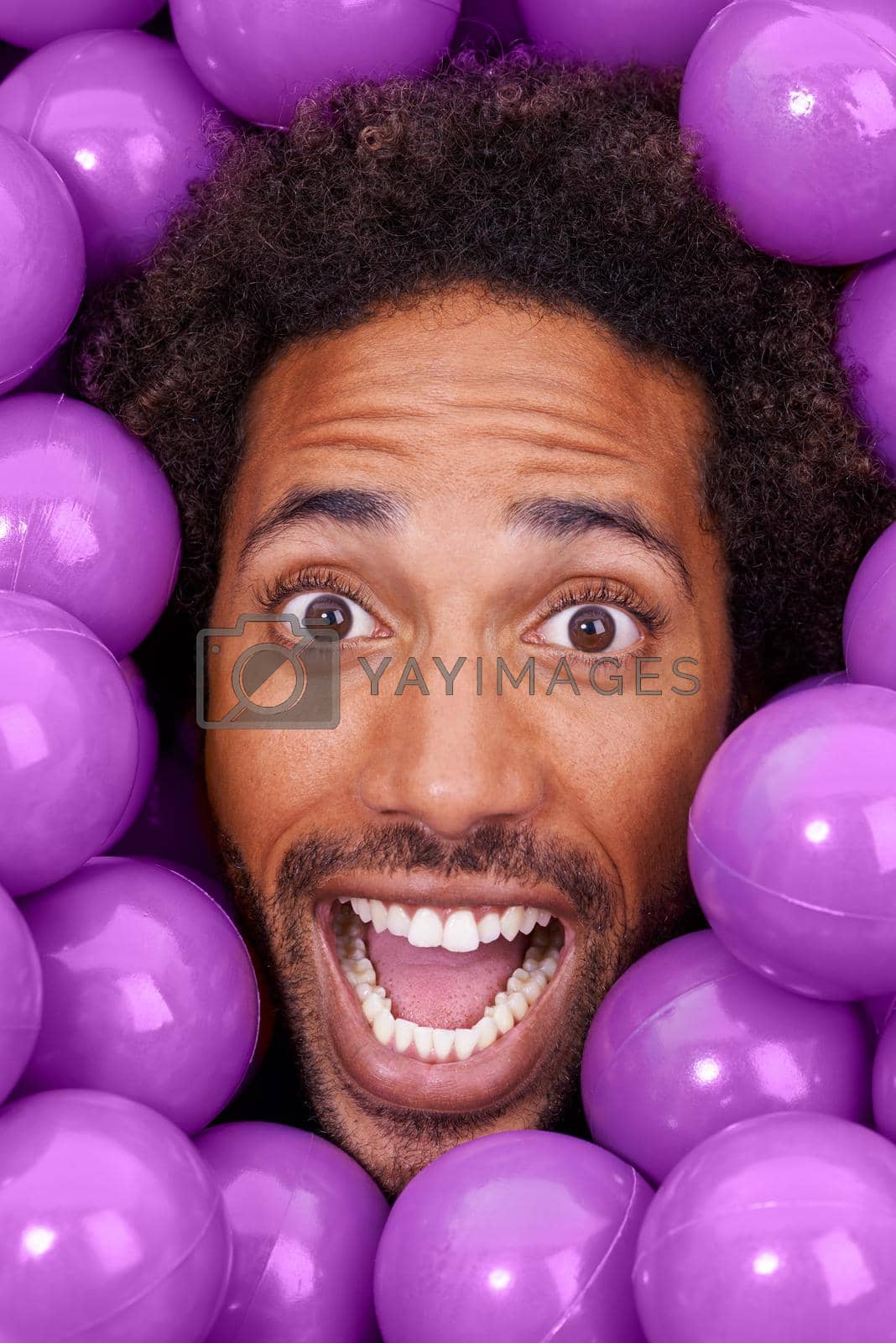 Royalty free image of Hey, this ball pit is crazy. A young black mans face amongst purple pit balls. by YuriArcurs
