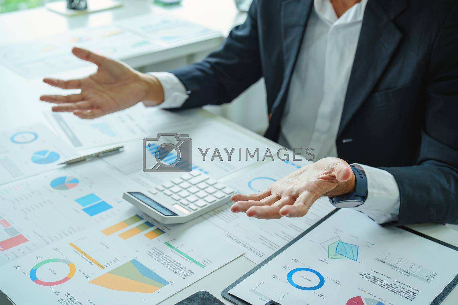 Royalty free image of A male businessman or marketer gestures to explain an action plan to increase profits to the audience using the financial and investment budget document with a calculator in the conference room by Manastrong