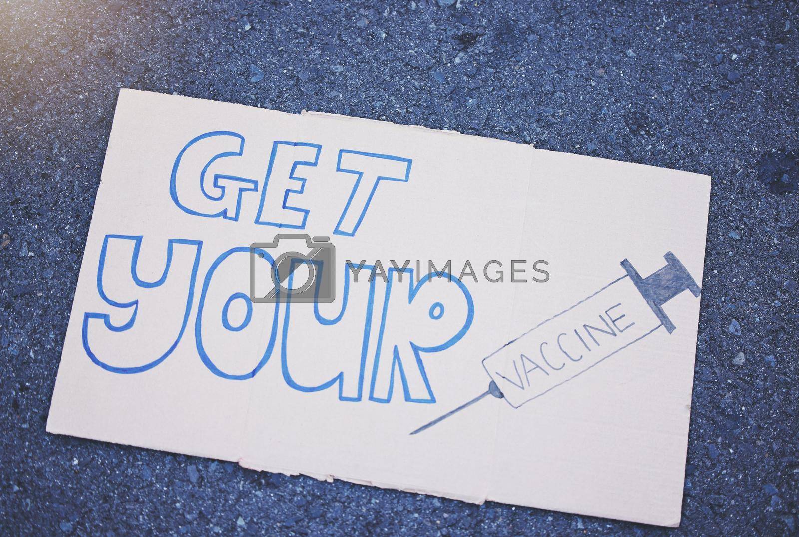 Royalty free image of Covid, vaccine and poster with a sign on the ground outside during the corona virus pandemic. Propaganda, motivation and advertising with writing on a board for vaccination, healthcare and medicine by YuriArcurs