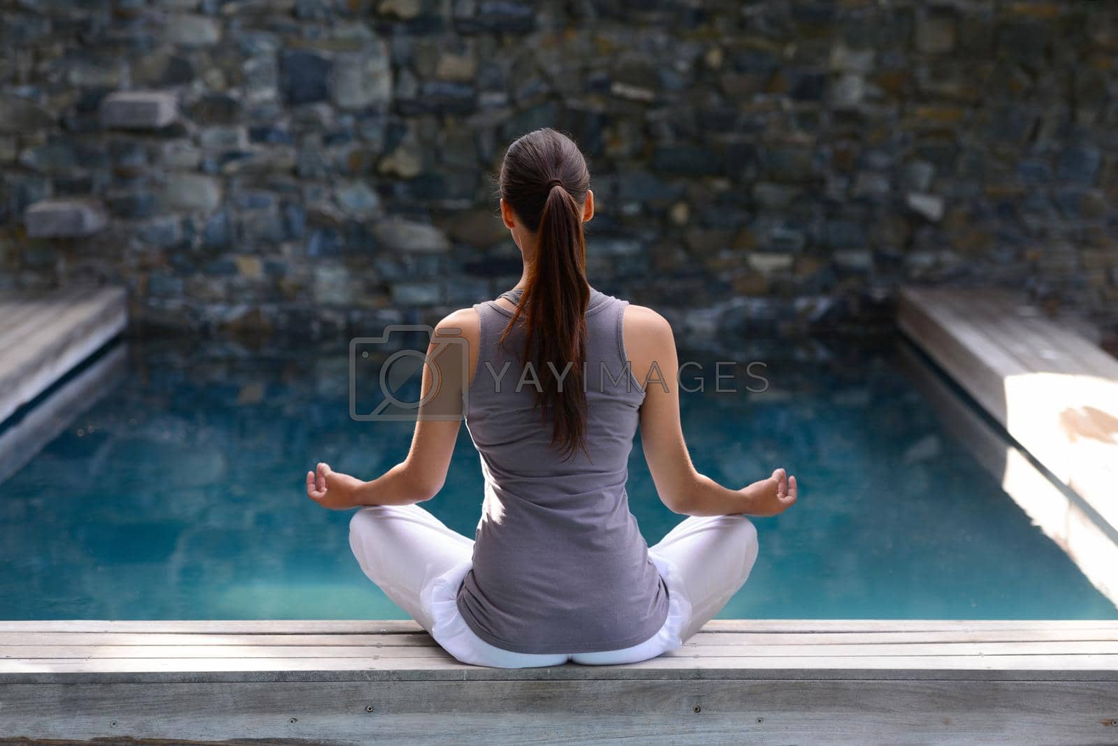 Royalty free image of Inner reflection. Rear view shot of a young woman meditating by a pool. by YuriArcurs