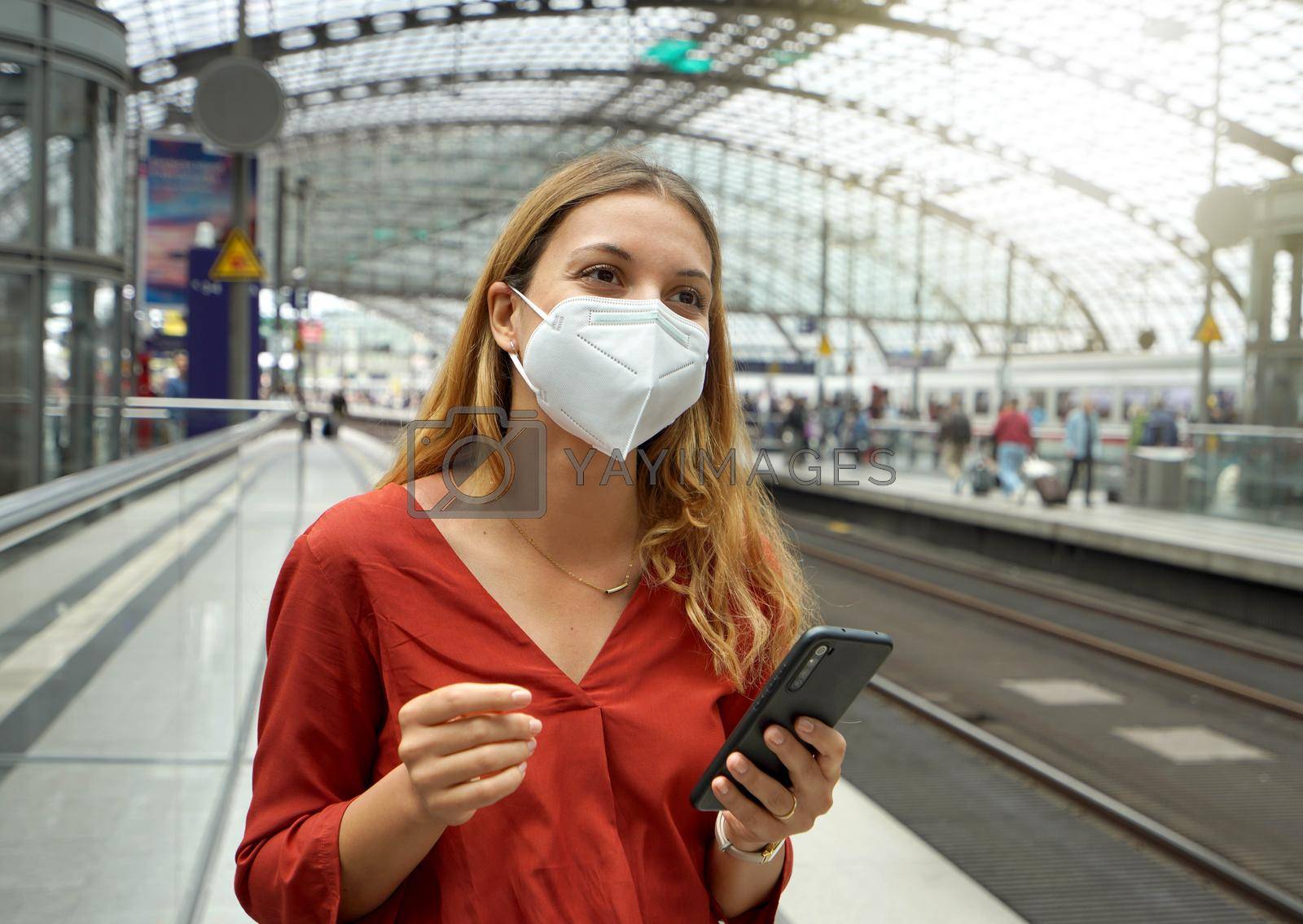 Traveler woman wearing KN95 FFP2 face mask at the airport train station. Young caucasian woman waiting shuttle train to the airport.