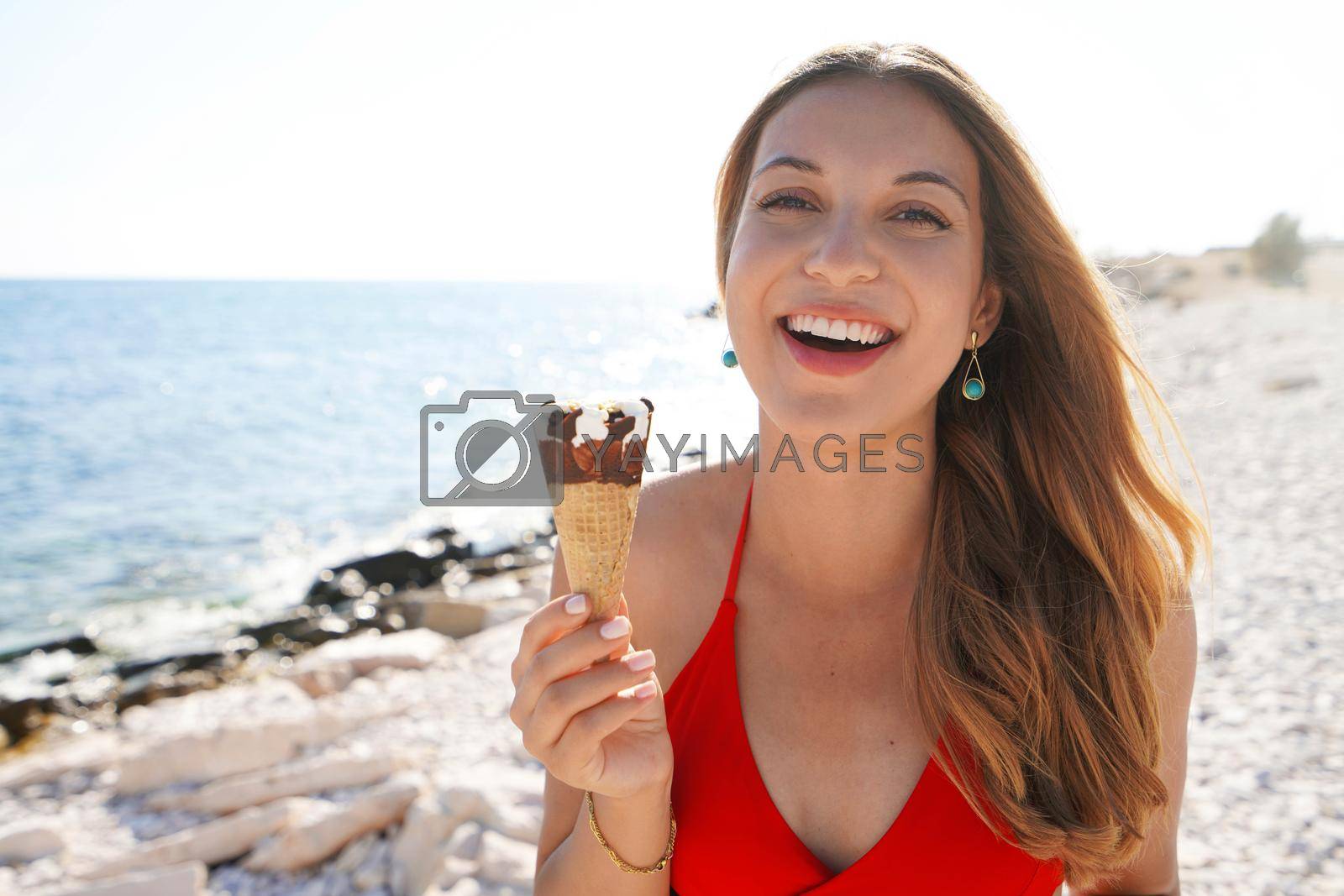 Royalty free image of Beautiful young woman smiling with ice cream cone looking at camera on beach by sergio_monti