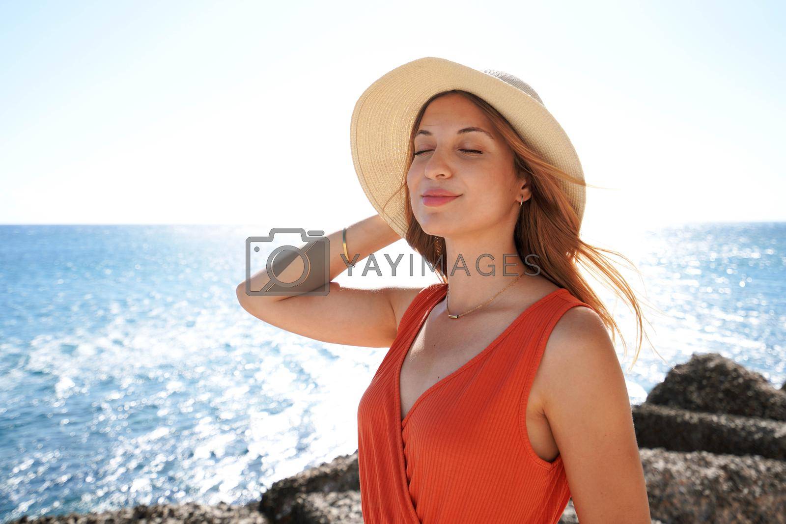 Portrait of young fashion woman enjoying fresh air on face on her luxury vacation resort on beach. Summer holidays and relax concept