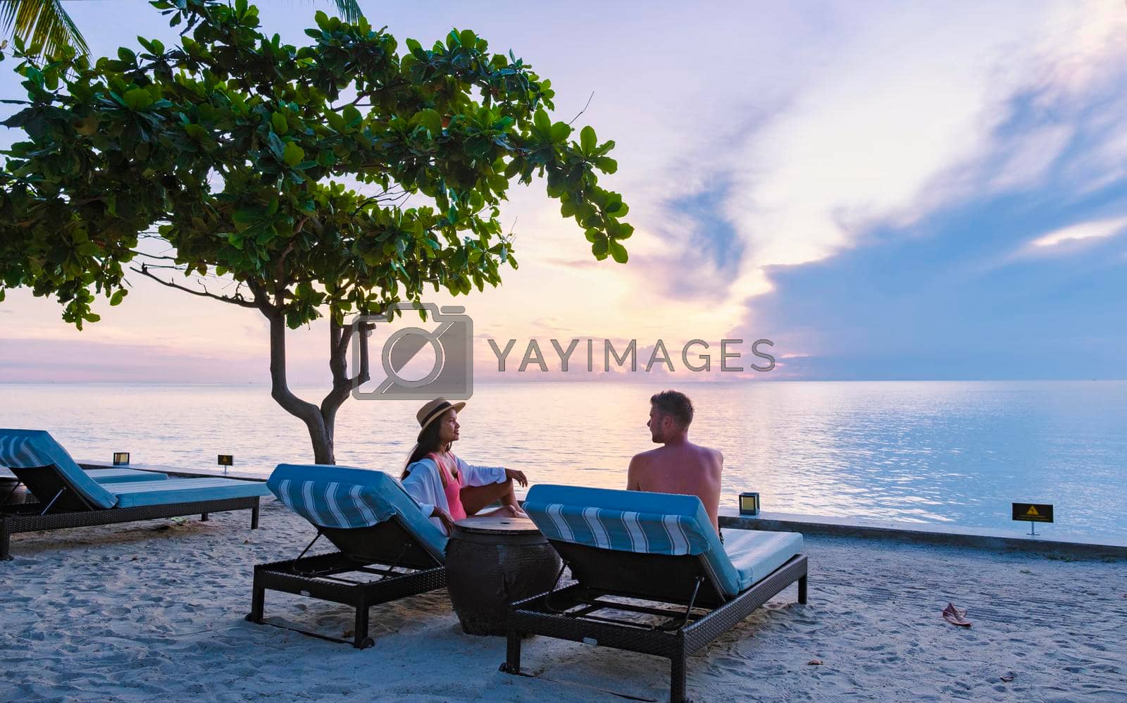 Royalty free image of Couple of men and women relaxing by the pool in beach beds chairs, tropical pool by fokkebok