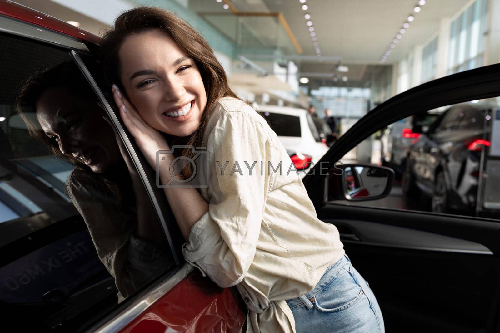 Royalty free image of young woman rejoices in buying a new car in a car dealership by TRMK