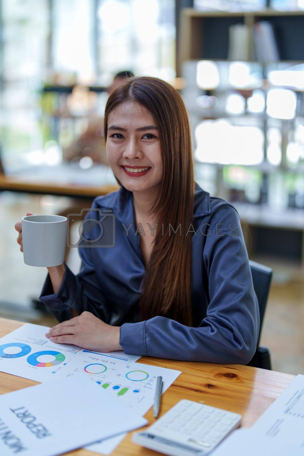 Royalty free image of Portrait of a happy Asian woman smiling at her desk during the daytime coffee break by Manastrong