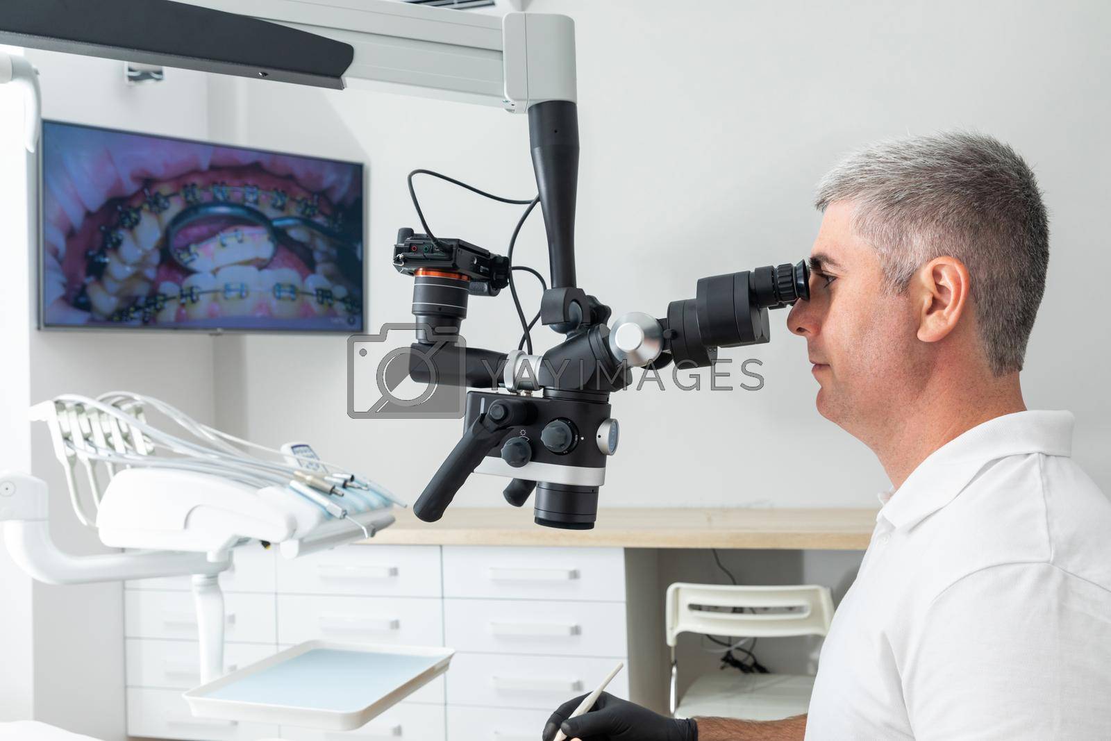 Male dentist using dental microscope treating patient teeth at dental clinic office. Medicine, dentistry and health care concept