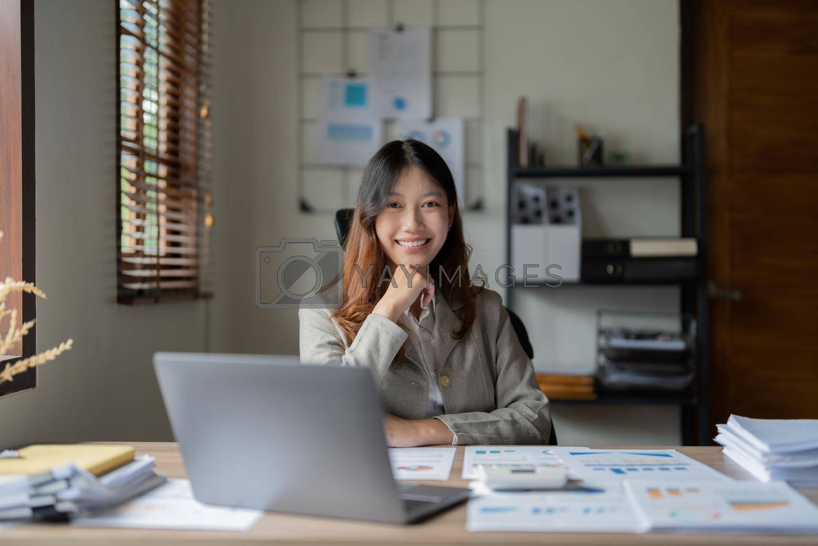 Royalty free image of Portrait pretty asian businesswoman smiles at the camera while sitting at her desk in front of the laptop computer by nateemee