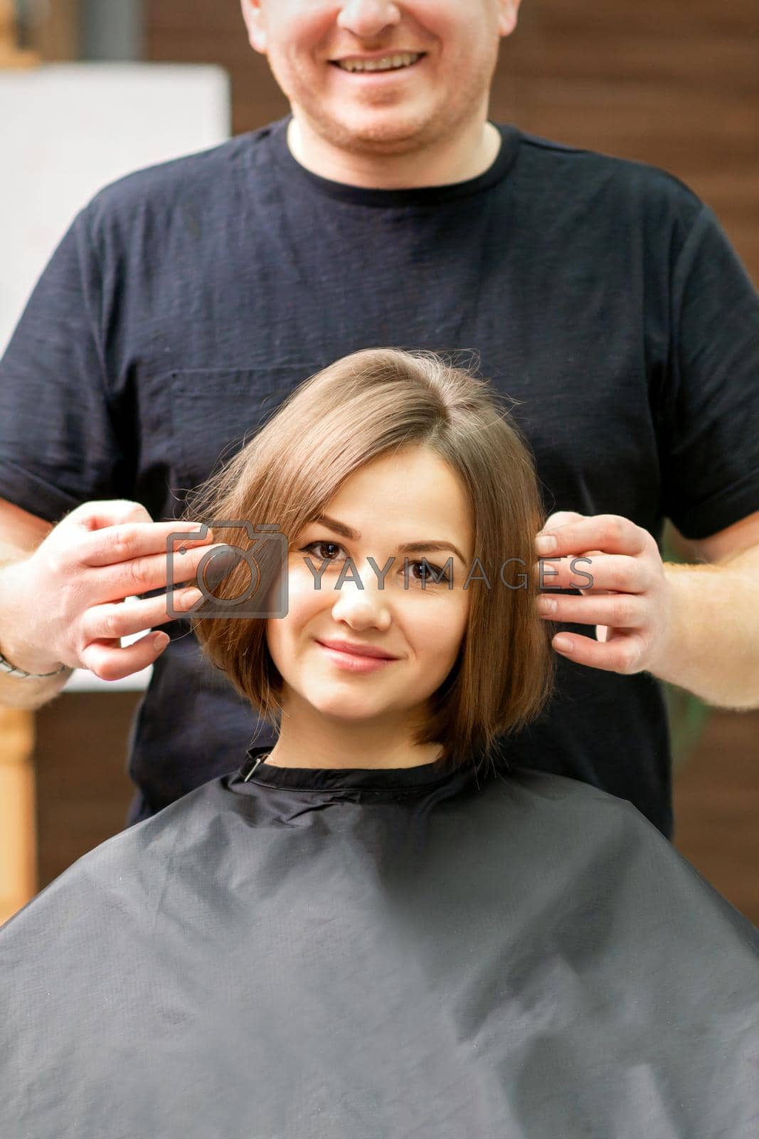 Royalty free image of Gorgeous brunette short hair woman and her male hairdresser looking and checking out hairstyle. Beautiful hairstyle of a young brunette woman, results of hair treatment in a beauty salon. by okskukuruza