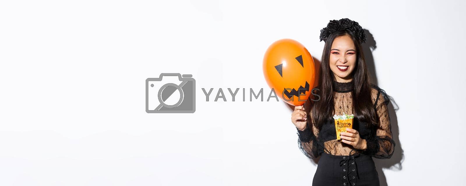 Royalty free image of Sassy beautiful asian woman enjoying trick or treating, celebrating halloween, holding orange balloon and sweets by Benzoix