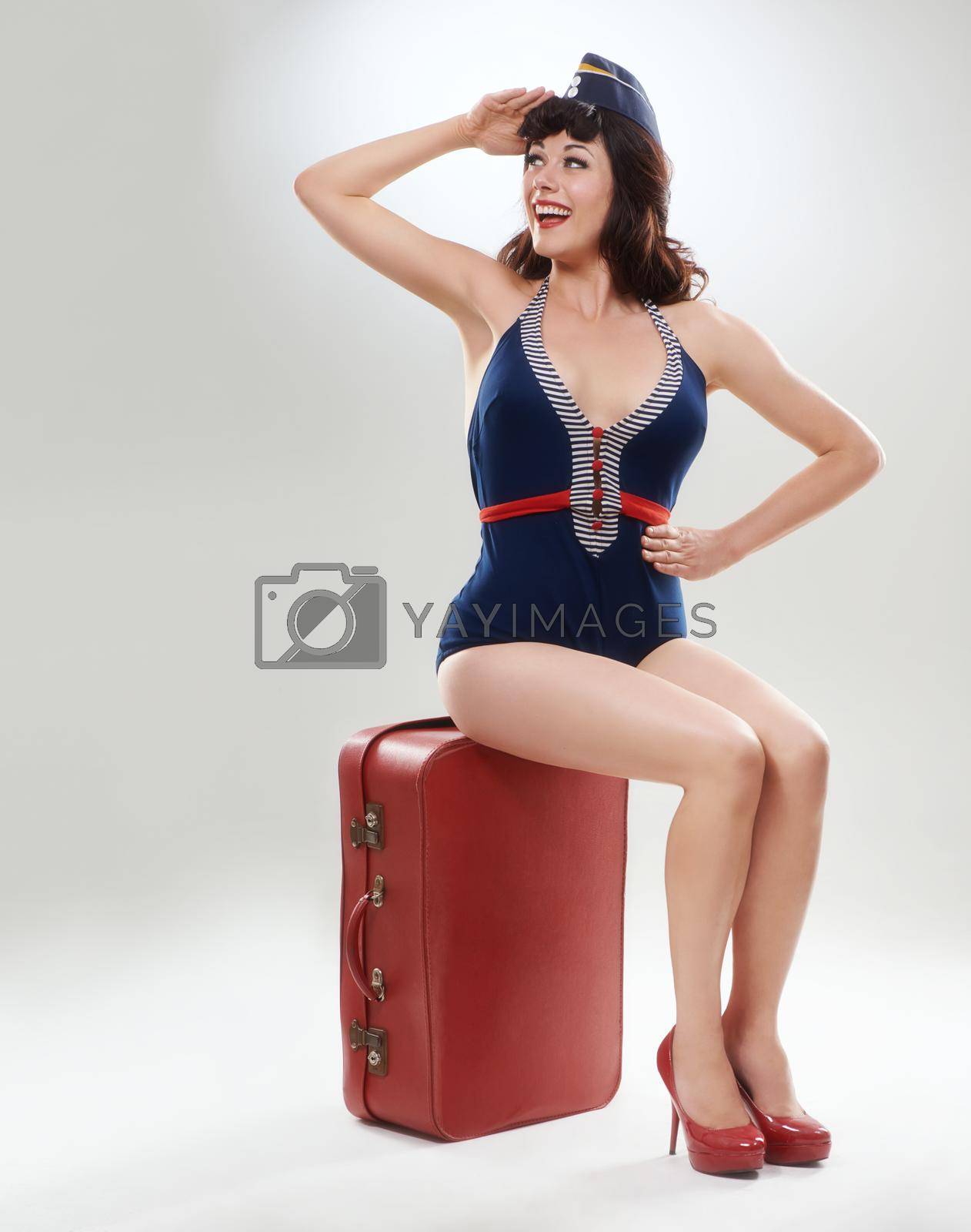 Royalty free image of Dreaming about her travels. A retro flight attendant sitting on a red suitcase. by YuriArcurs
