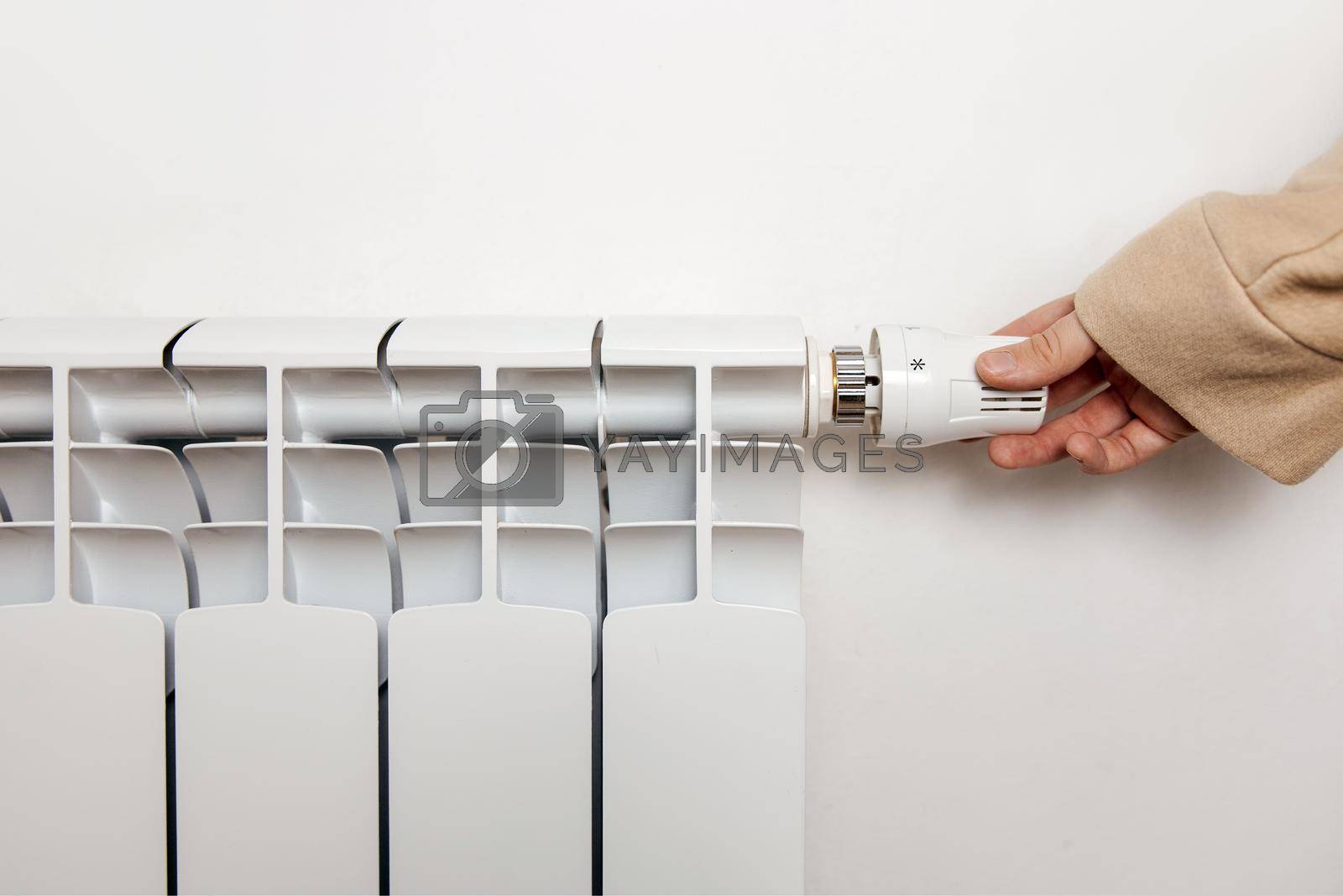 Royalty free image of White heating radiator hanging on white wall, close up view. Person turns on or turns off radiator. Central heating system. Heating is getting more expensive, save money. Energy crisis. Copy space. by creativebird
