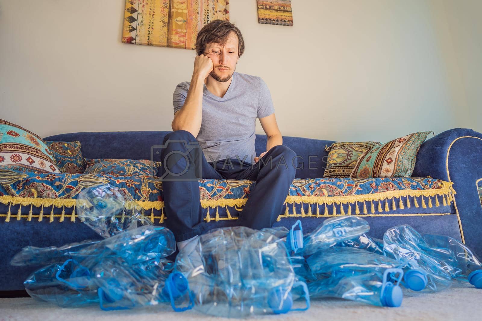 Royalty free image of Young caucasian man hamong empty plastic bottles to recycle with sad expression by galitskaya