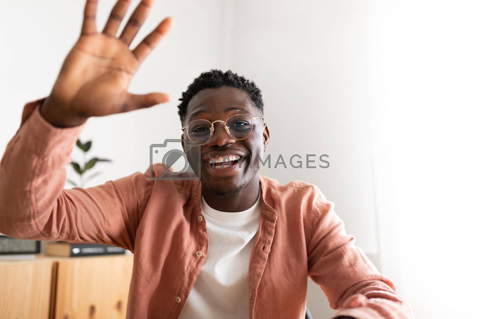 Royalty free image of African american young man looking at camera waving hand saying hello during video call. by Hoverstock