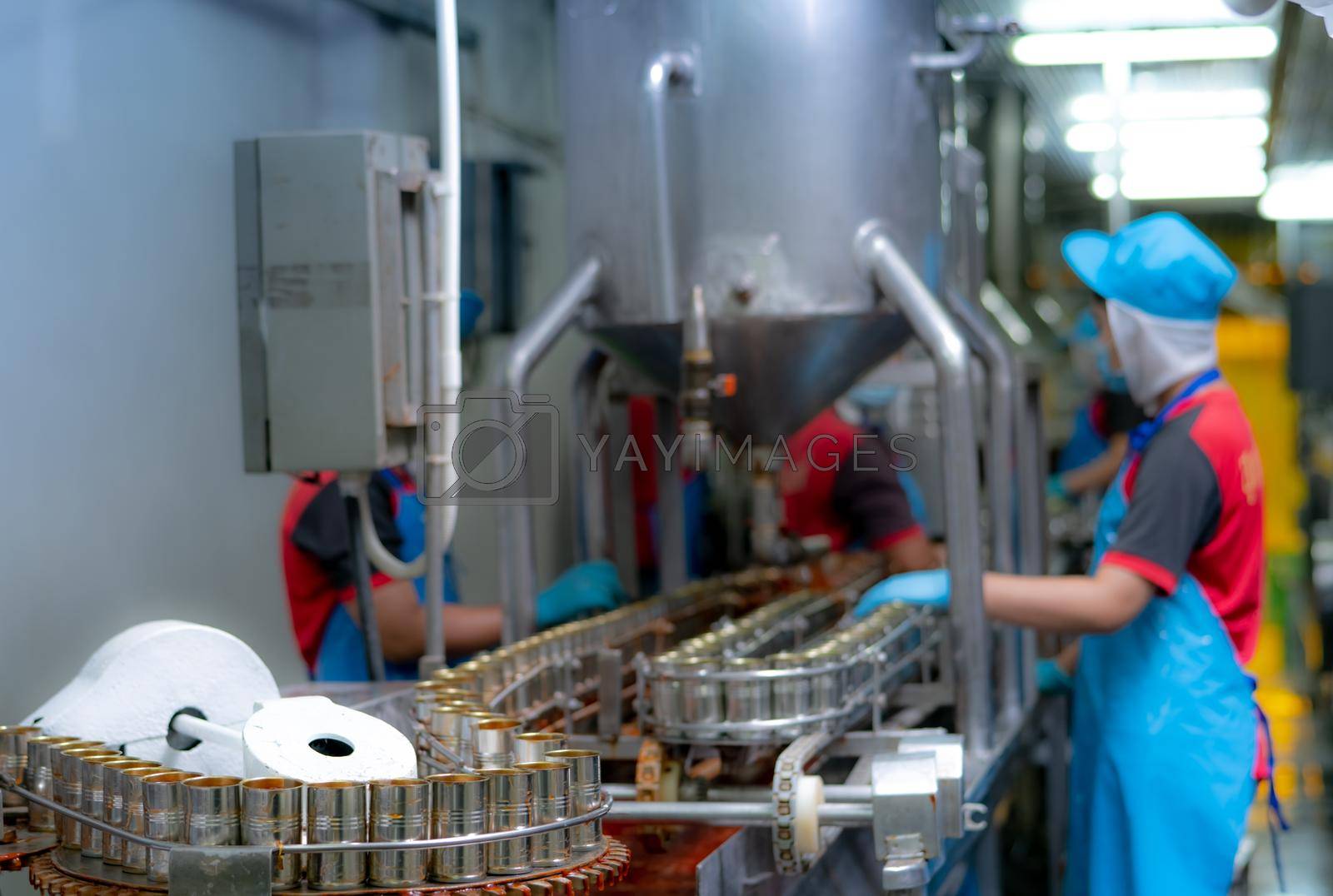 Royalty free image of Canned fish factory. Food industry.  Sardines in red tomato sauce in tinned cans on conveyor belt at food factory. Blur workers working in food processing production line. Food manufacturing industry. by Fahroni