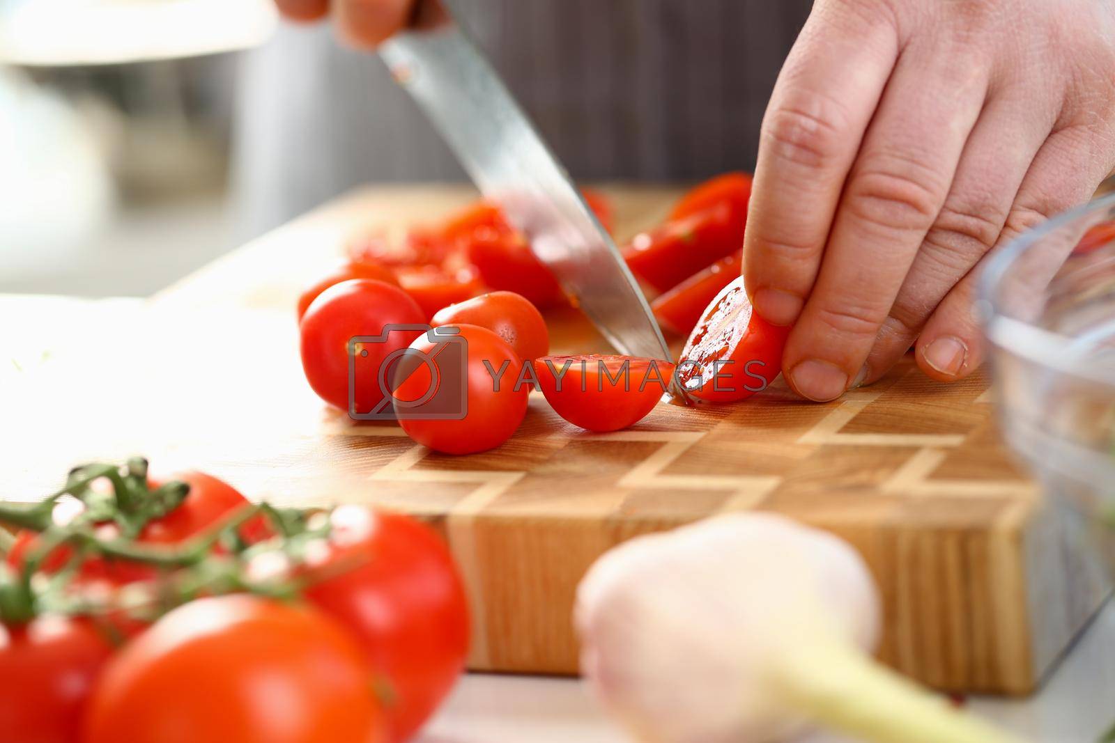 Royalty free image of Closeup of man hand cutting tomato on cutting board at home by kuprevich