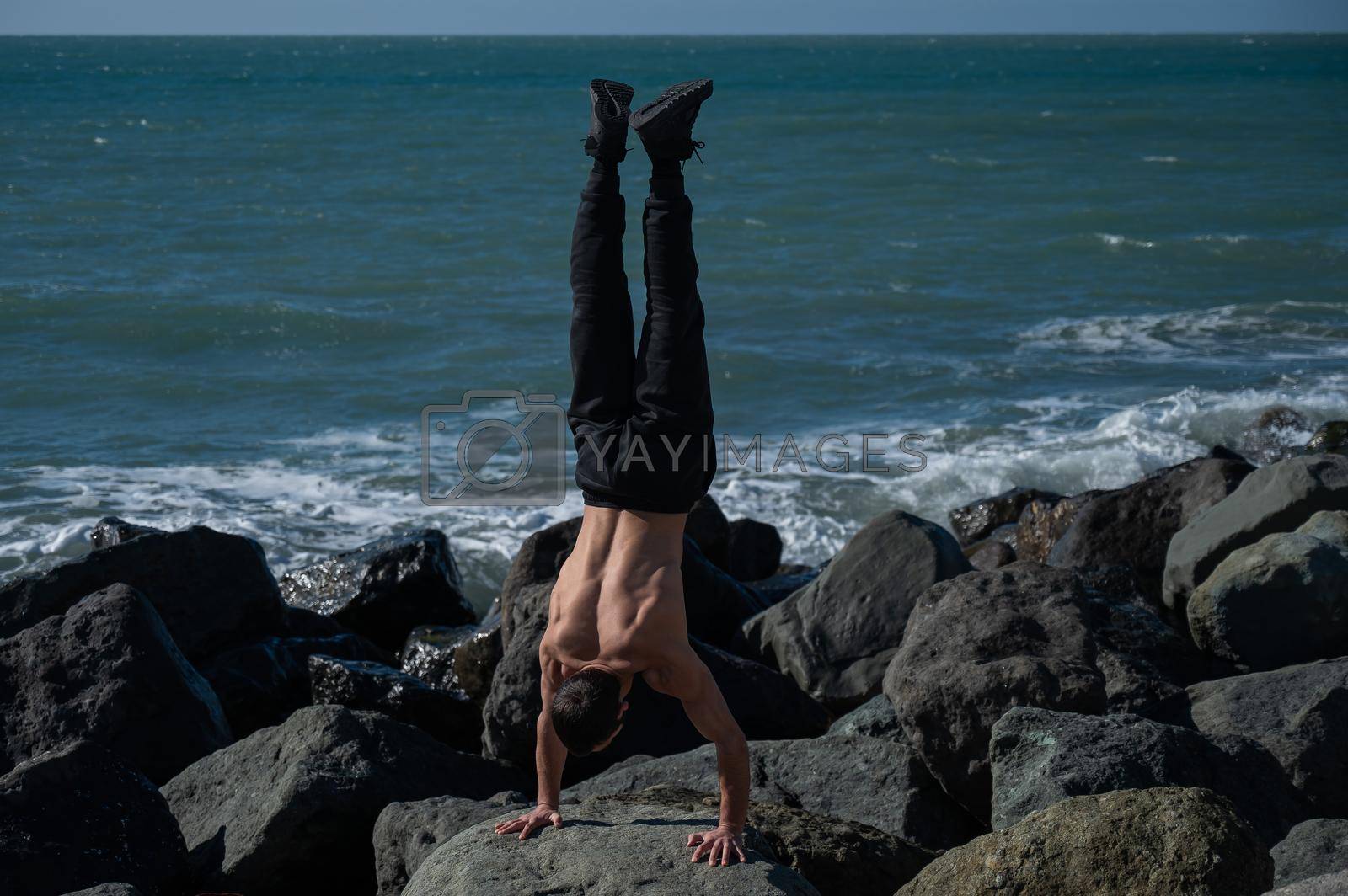 Royalty free image of Shirtless man doing handstand on rocks by the sea. by mrwed54