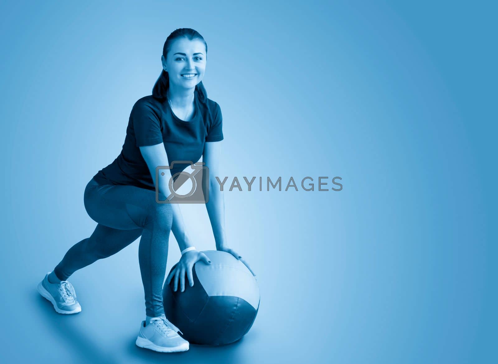 Royalty free image of woman in gym relaxing with medicine ball by Mariakray