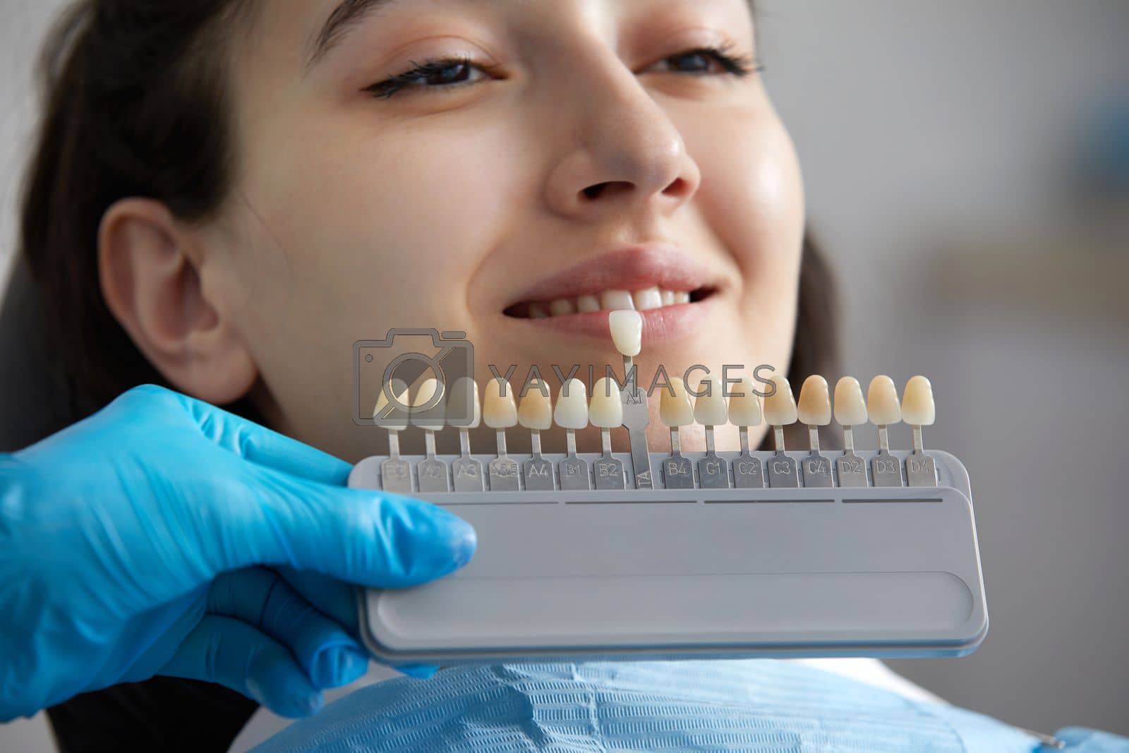 Royalty free image of Dentist choosing color of tooth enamel for patient. Dentist applying sample from tooth enamel scale to caucasian female teeth by Mariakray