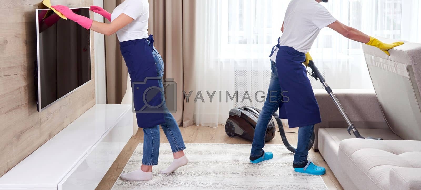 Royalty free image of Professional cleaners in blue uniform washing floor and wiping dust from the furniture in the living room of the apartment. Cleaning service concept by Mariakray
