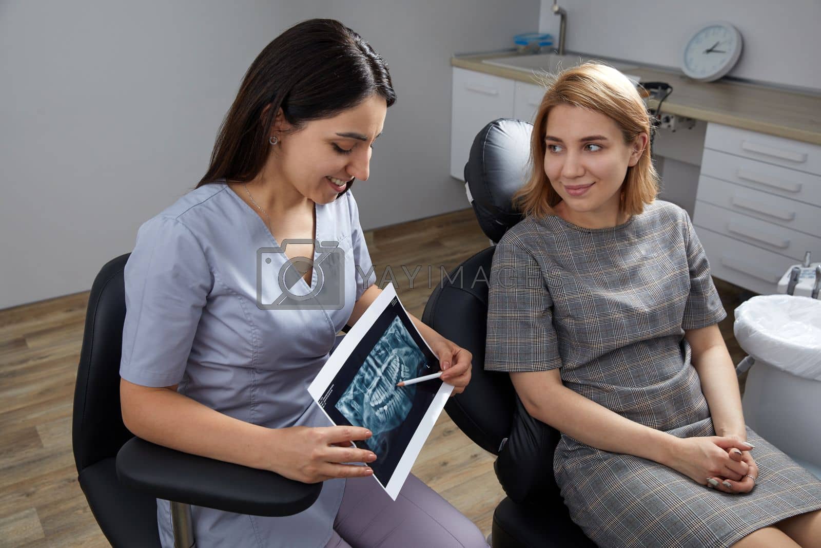 Royalty free image of Female dentist pointing at patient's X-ray image in dental office by Mariakray