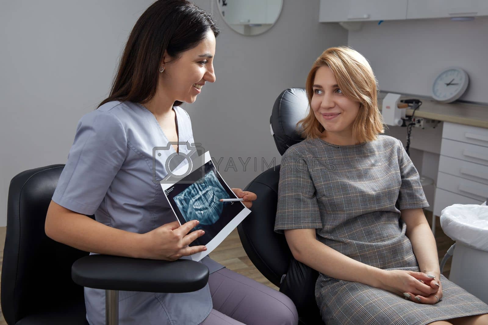Royalty free image of Female dentist pointing at patient's X-ray image in dental office by Mariakray