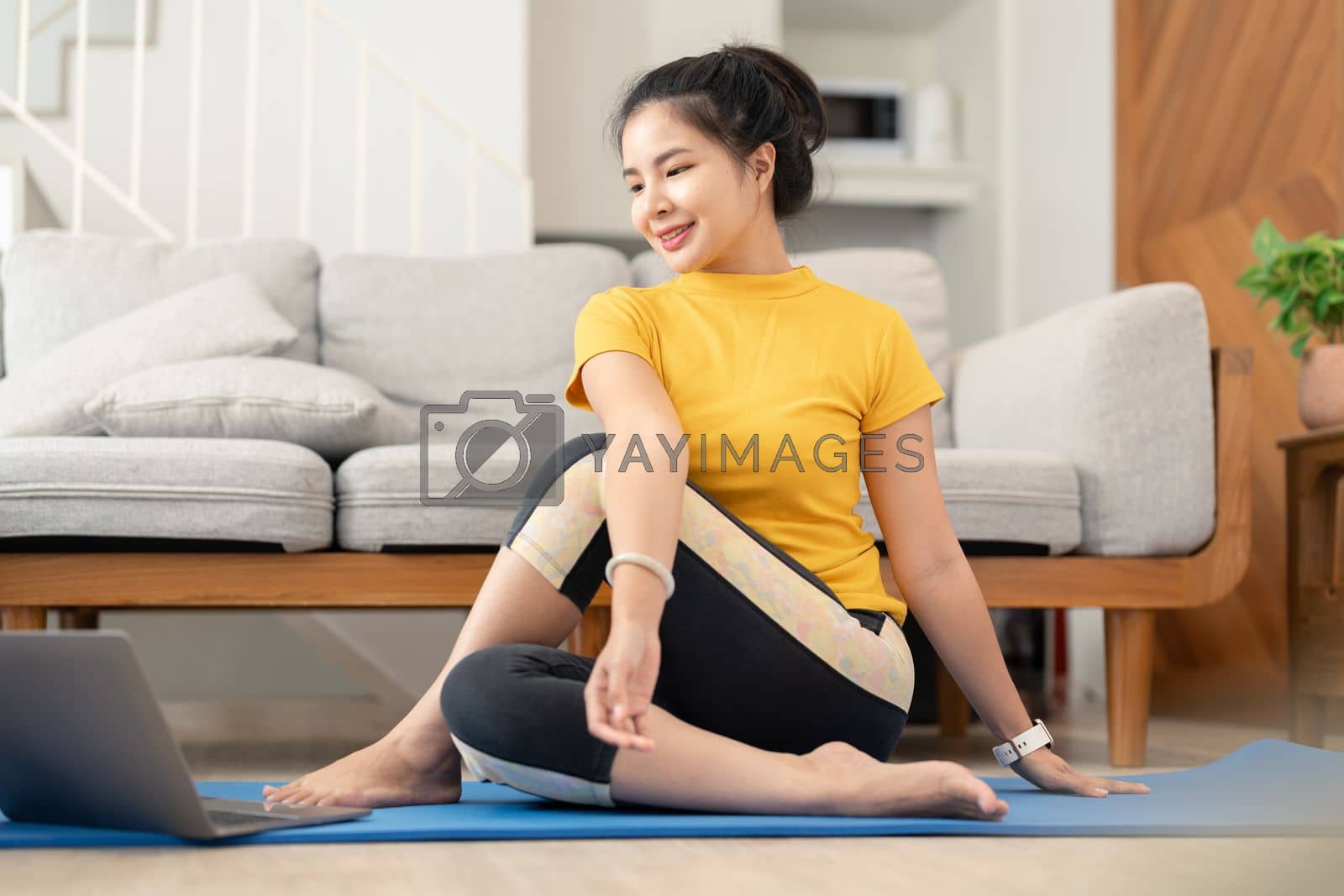 Royalty free image of Attractive young woman doing yoga stretching yoga online at home. Self-isolation is beneficial. Healthy lifestyle concept by nateemee