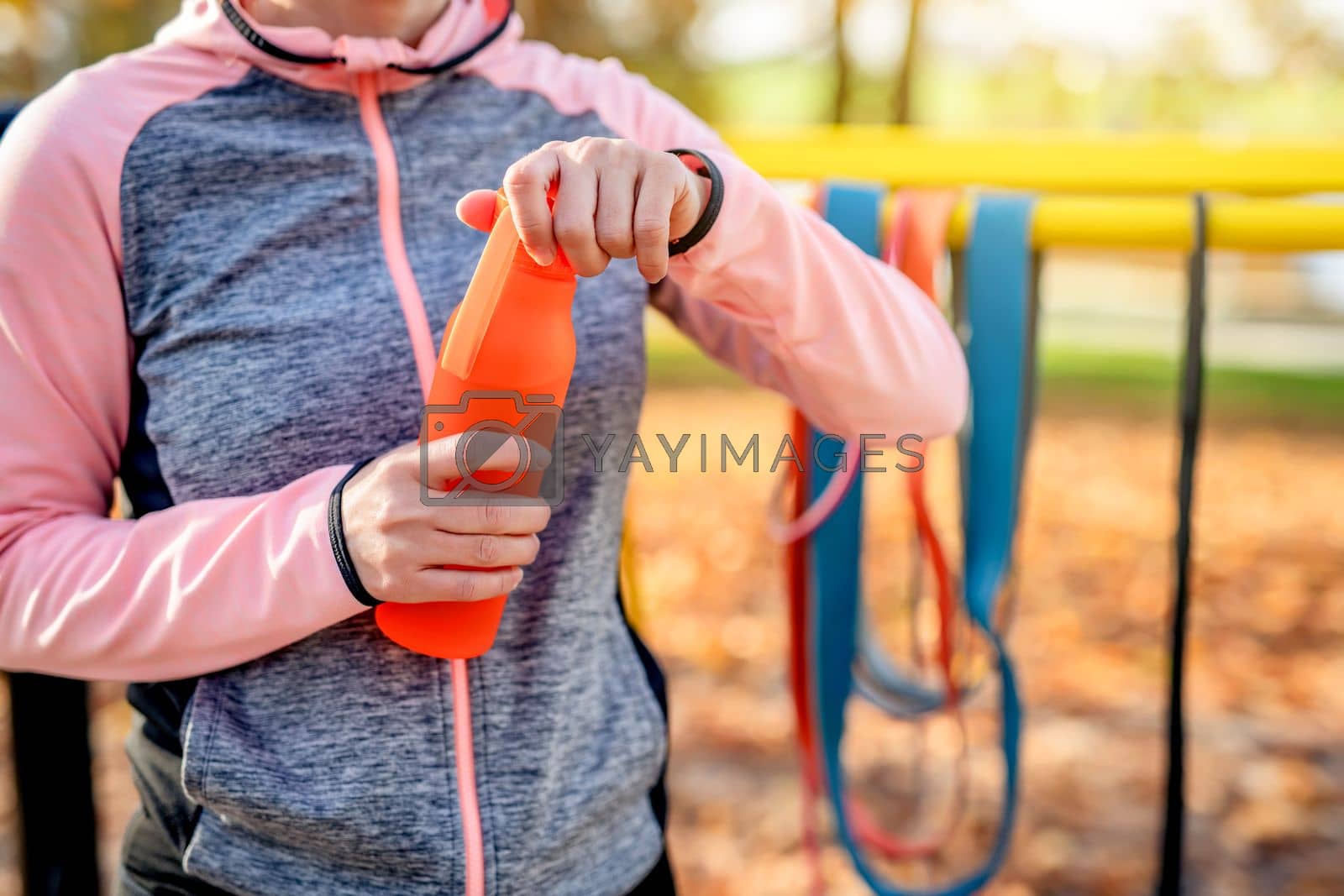 Fitness girl opening bottle with water after exercising in autumn park outdoors. Young woman and hydration during training at fall season