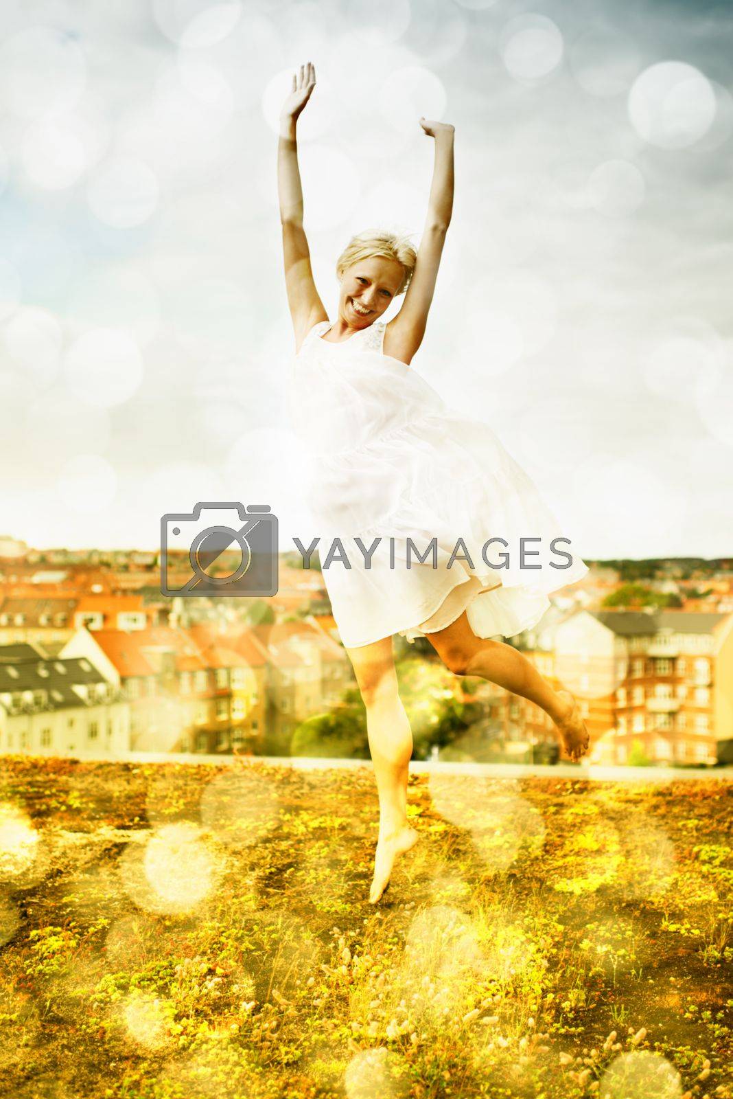 Royalty free image of Feeling free. Beautiful young woman jumping on a rooftop with a city in the background surrounded by bokeh. by YuriArcurs
