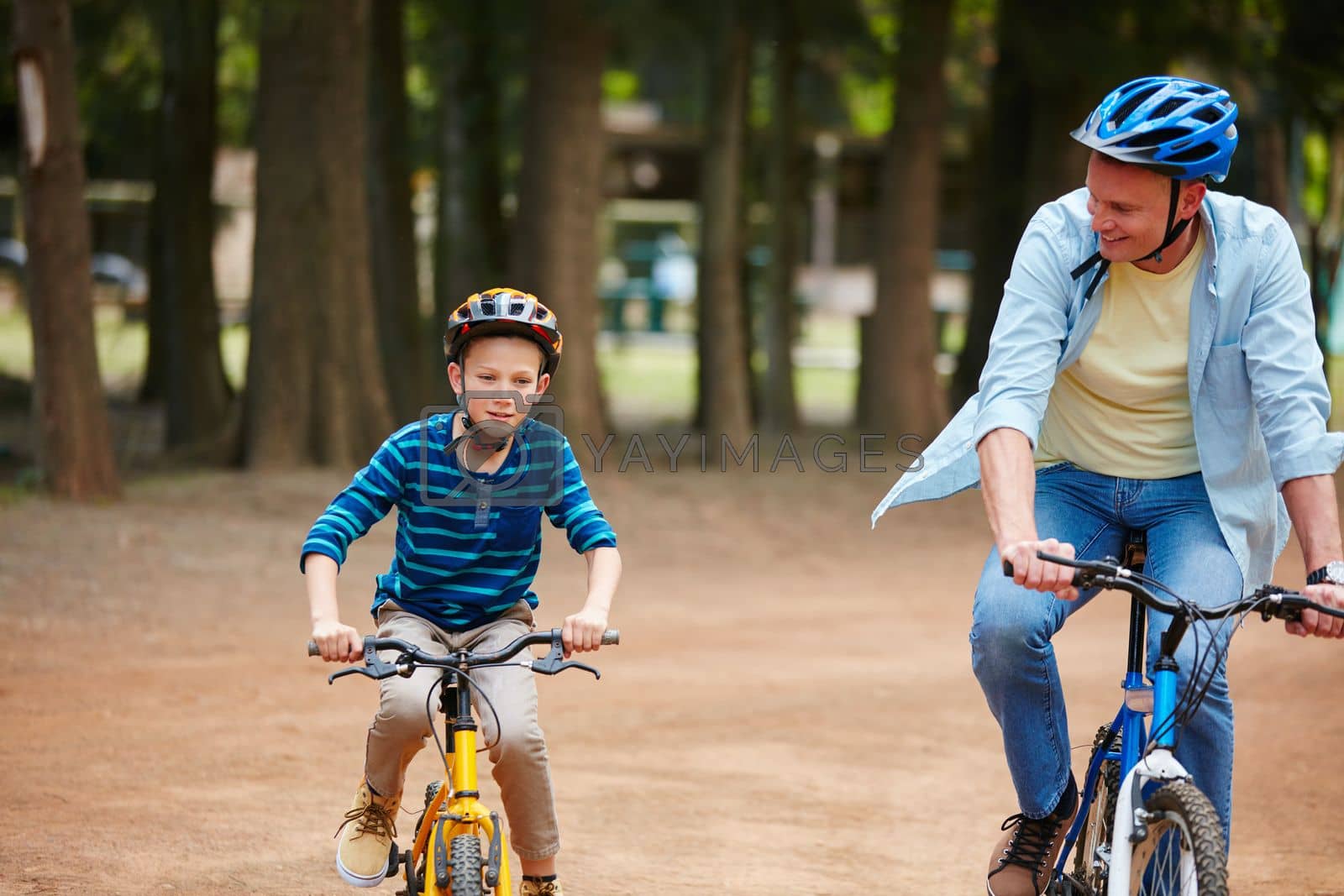 Royalty free image of You doing great son. a father and his young son riding bicycles through a park. by YuriArcurs
