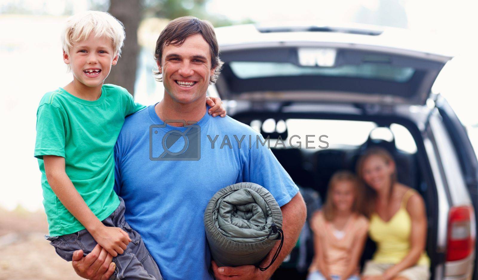 Royalty free image of Father carrying son. Portrait of father carrying son and smiling with family sitting in car. by YuriArcurs