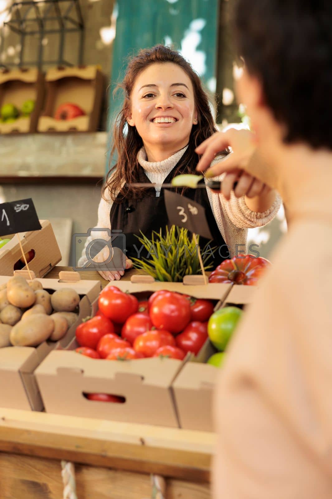 Royalty free image of Market vendor offering customer to taste locally-grown organic produce by DCStudio