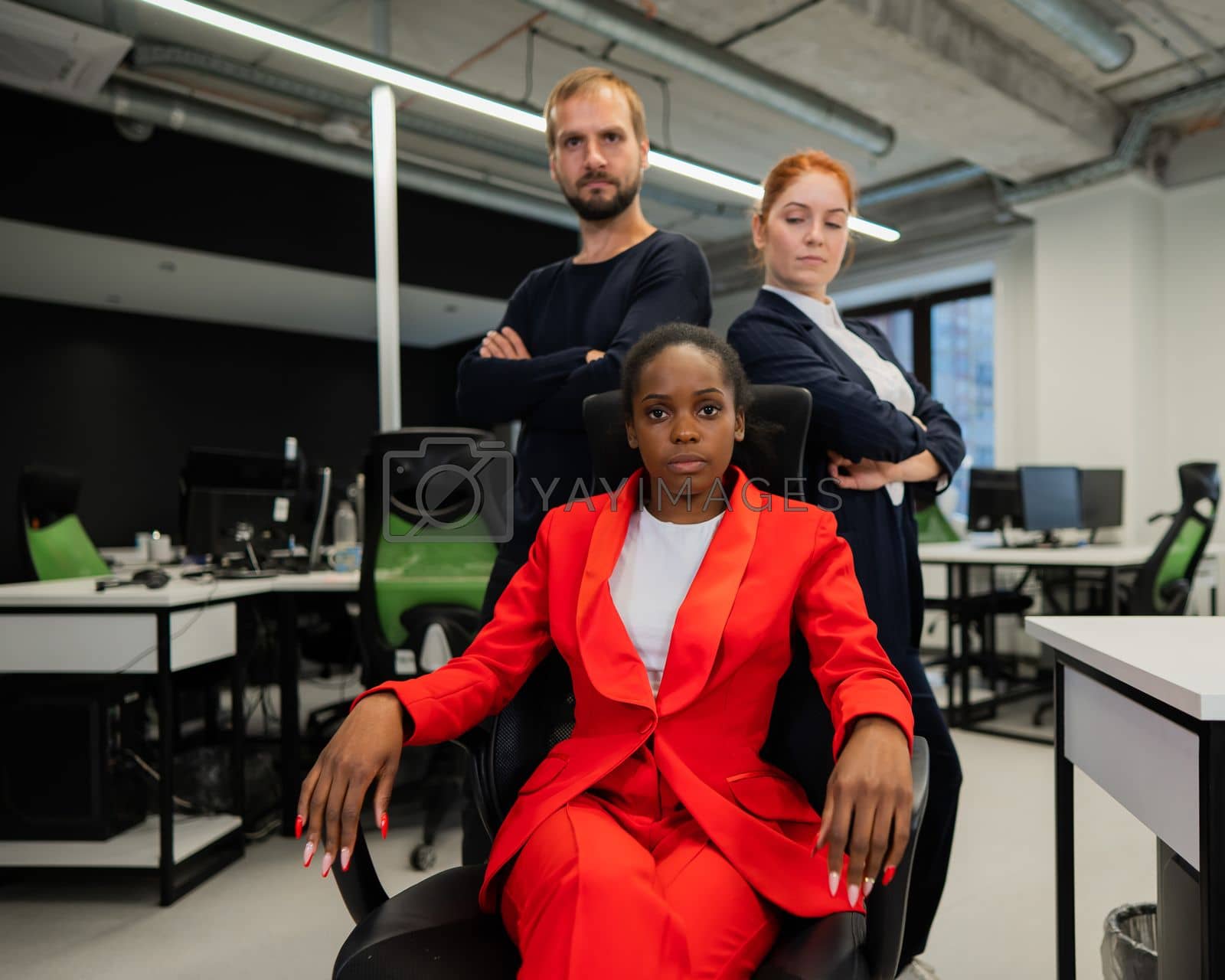 Royalty free image of Caucasian red-haired woman, bearded Caucasian man stand behind a seated African American young woman in the office. by mrwed54