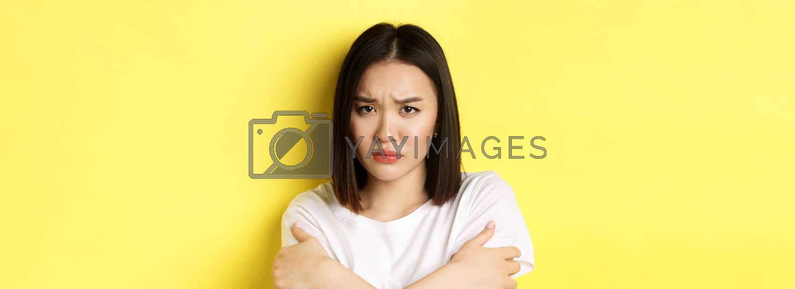 Royalty free image of Sad timid girl comforting herself, hugging body and frowning upset, standing again yellow background by Benzoix