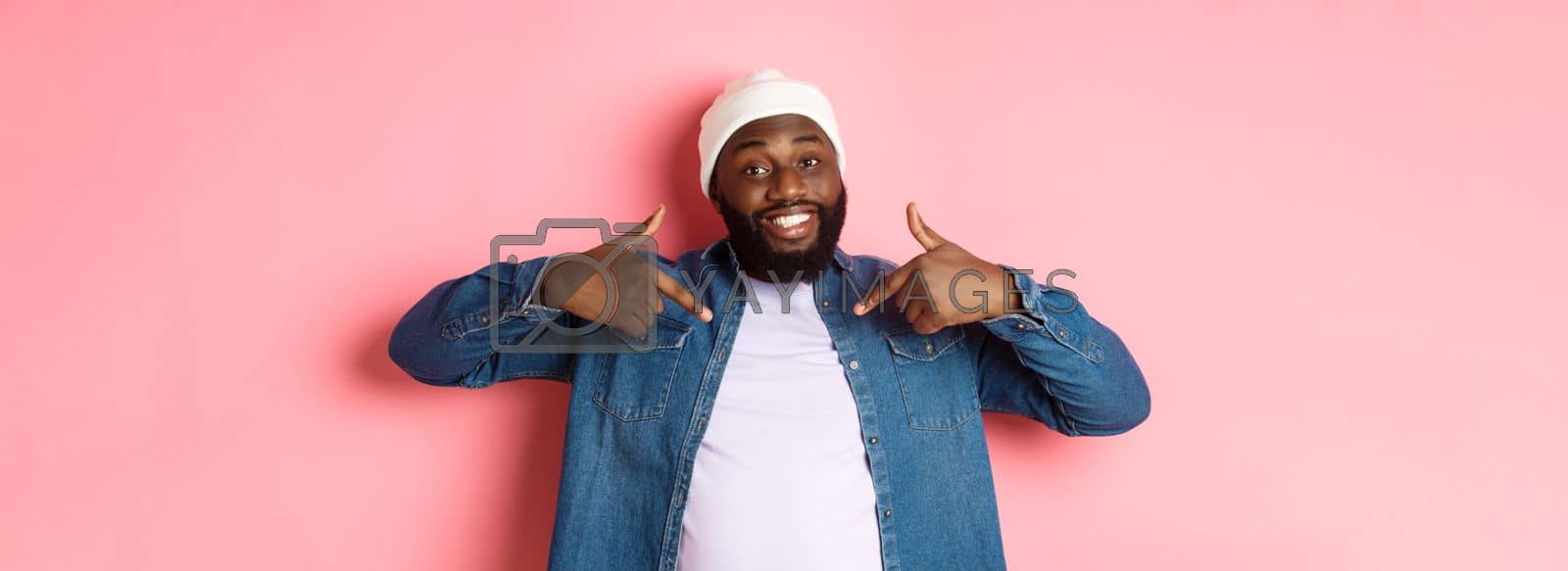 Royalty free image of Happy young african-american hipster guy pointing at himself t-shirt, smiling pleased, standing over pink background by Benzoix
