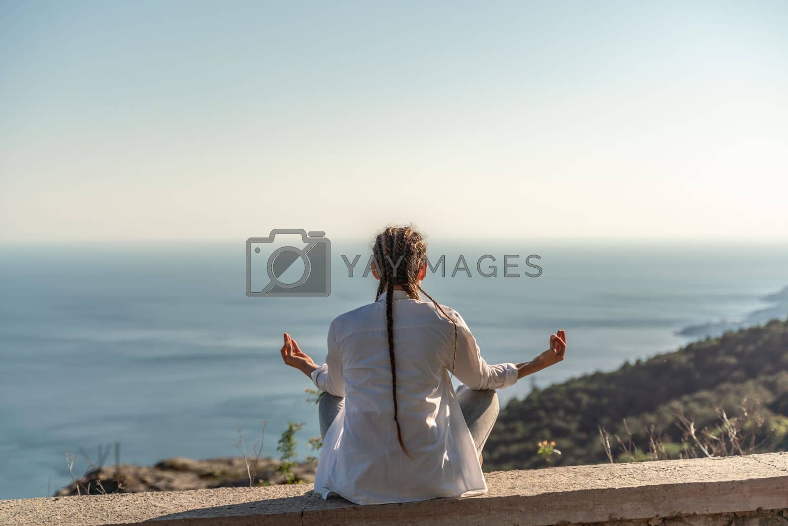 Royalty free image of woman doing yoga in the top of a cliff in the mountain. Woman meditates in yoga asana Padmasana by Matiunina