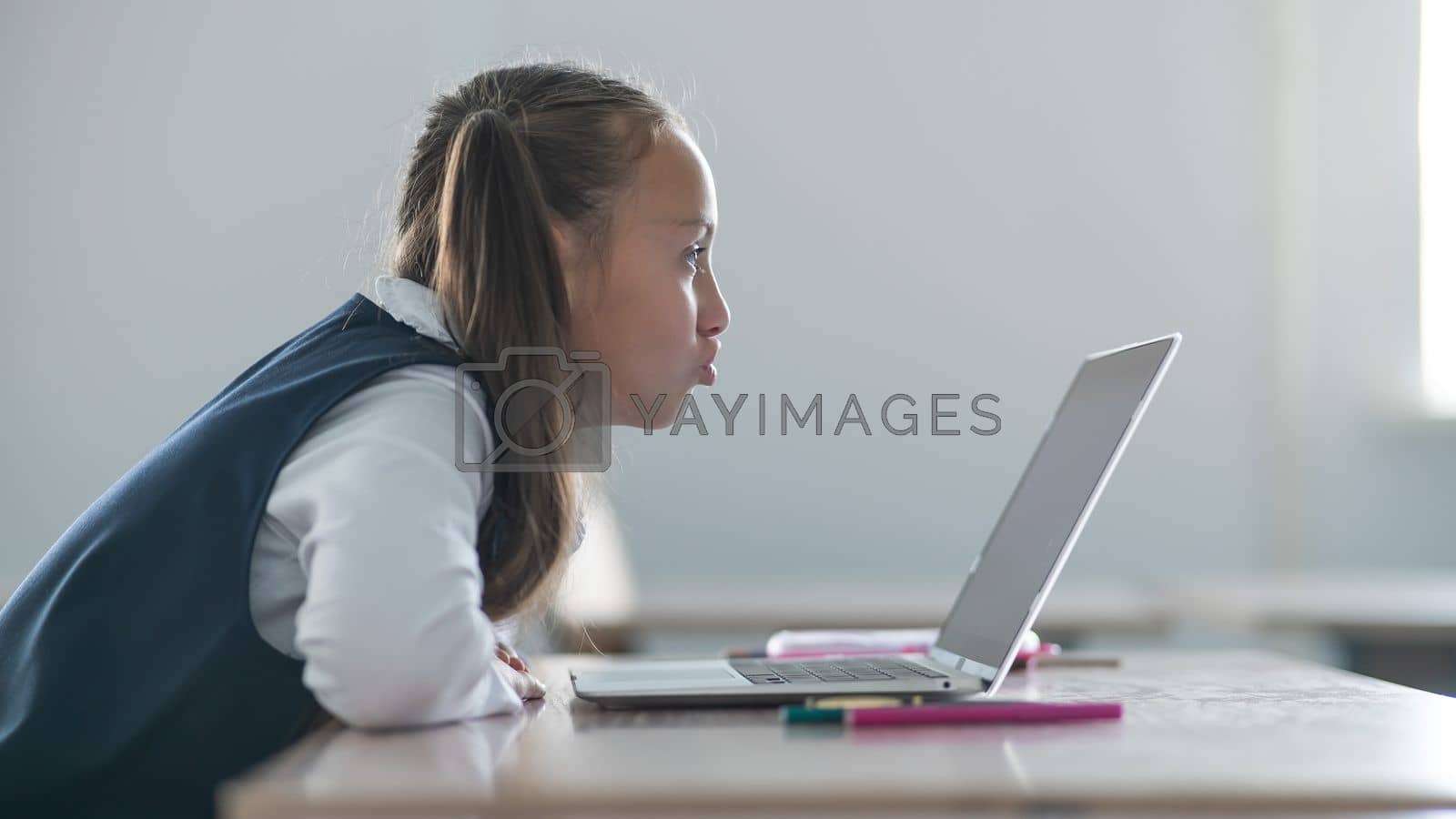 Caucasian girl communicates via video communication on a laptop while sitting at a school desk