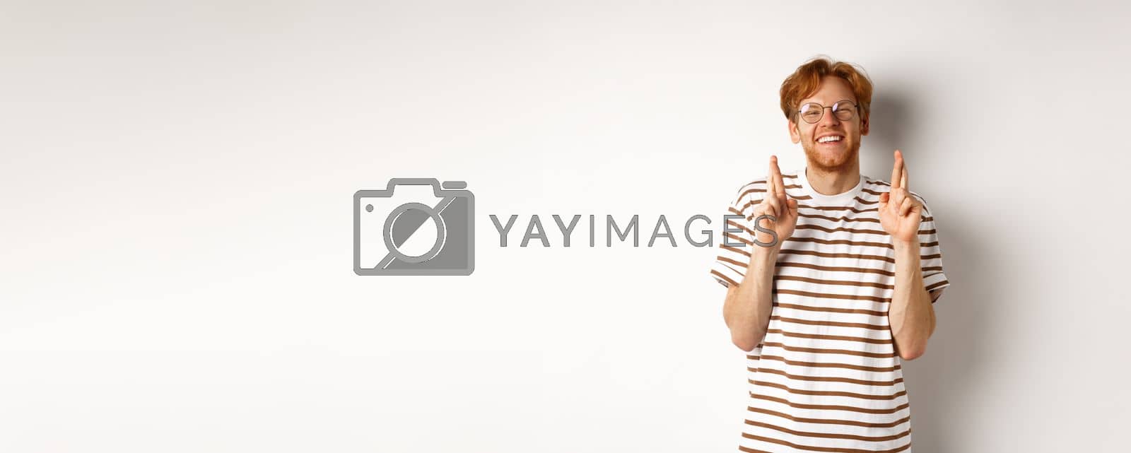 Royalty free image of Happy redhead man with bristle cross fingers for good luck and smiling hopeful, making wish, standing over white background by Benzoix