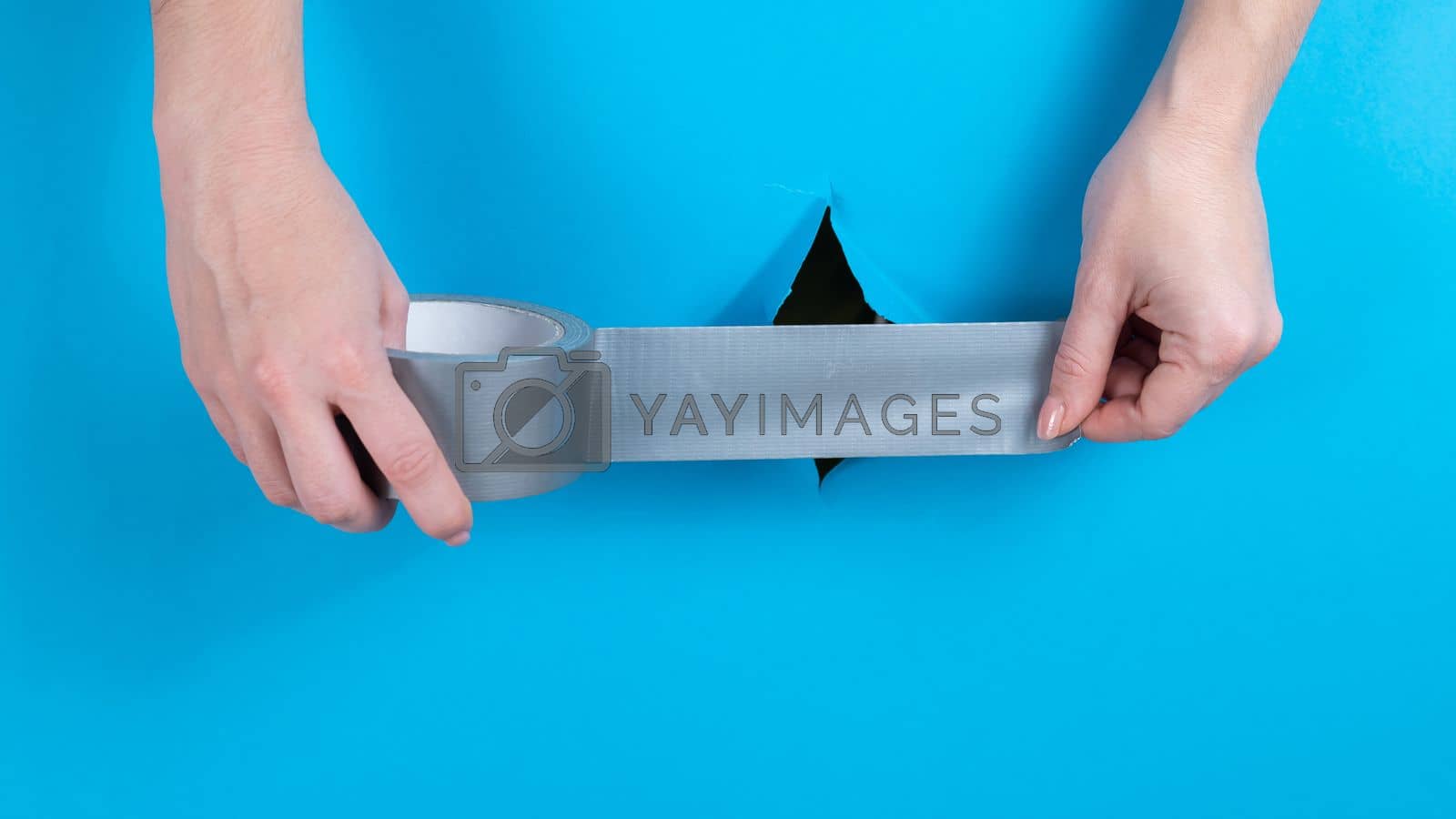 Royalty free image of Woman sticking silver tape on a hole on a blue background.  by mrwed54