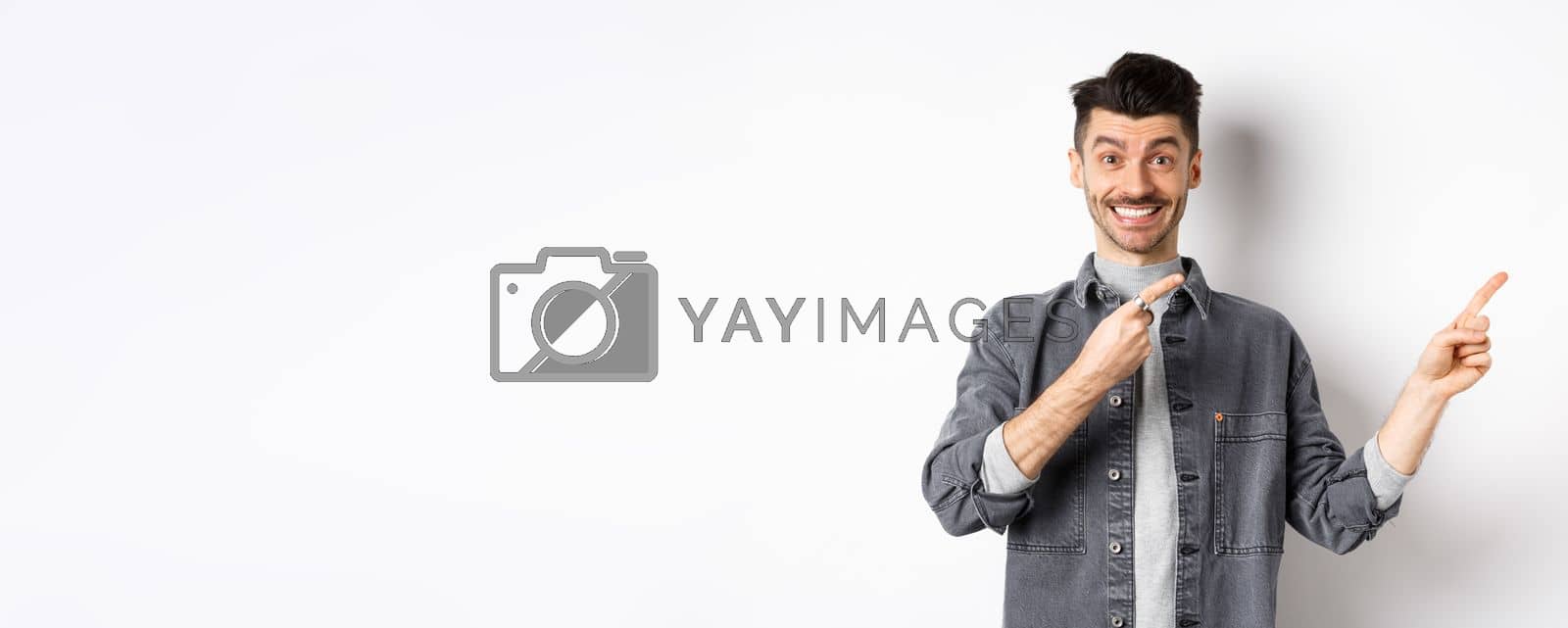 Royalty free image of Cheerful stylish man with moustache and white smile, pointing fingers right, inviting to look here, standing on white background by Benzoix