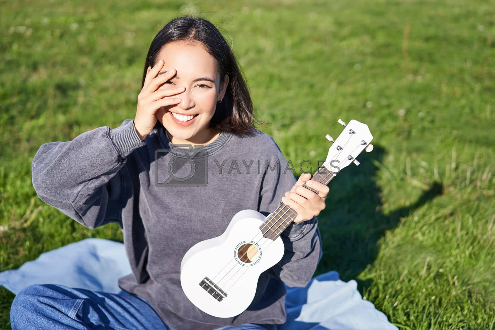 Royalty free image of Smiling asian girl with ukulele, playing in park and singing, lifestyle concept by Benzoix