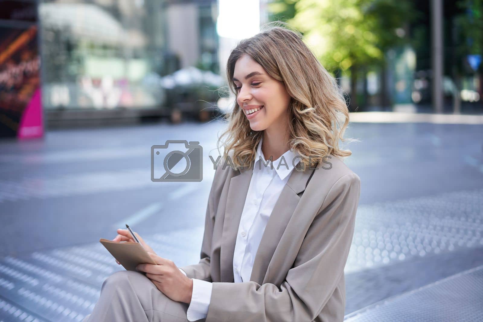 Royalty free image of Young businesswoman preparing for speech, interview in company, writing down notes while sitting outside in city centre by Benzoix